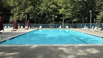 Ein Schwimmbecken mit Liegestühlen und Sonnenschirmen, umgeben von Bäumen.