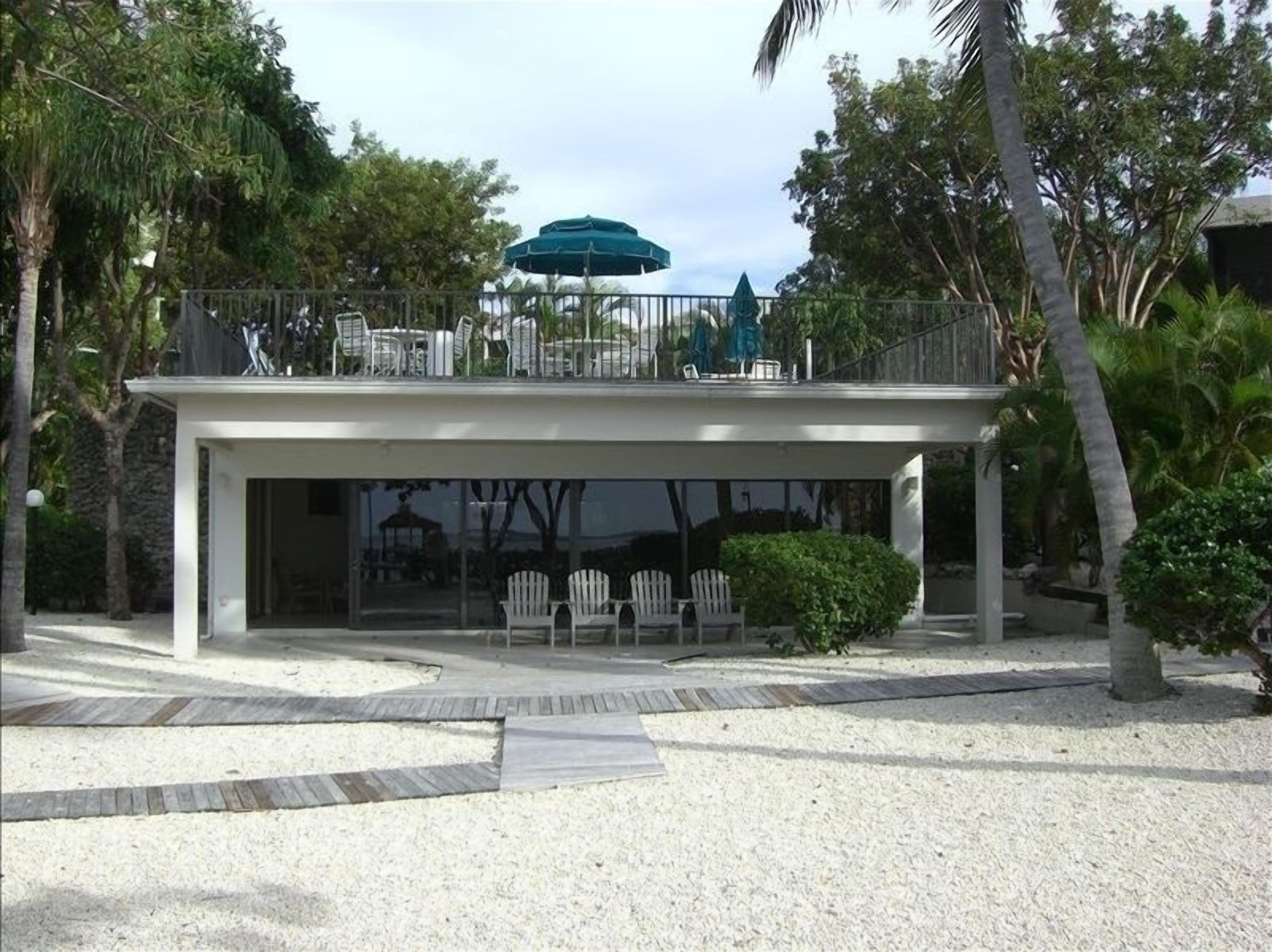 A modern building with a covered outdoor seating area, white chairs, and a green umbrella.