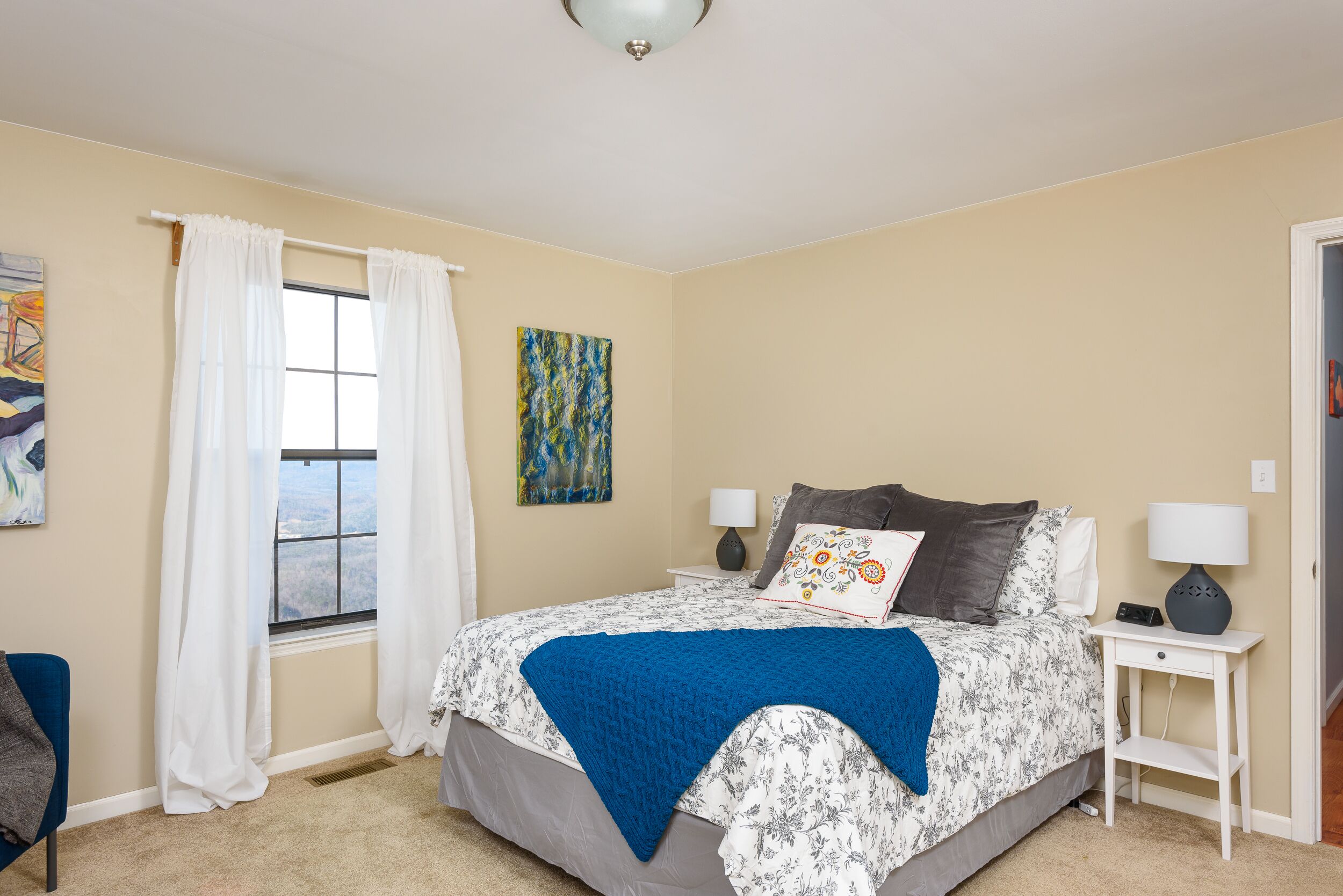 Une chambre à coucher avec un lit, deux tables de chevet, une fenêtre avec des rideaux et un tableau au mur.