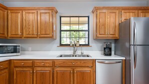 Una cocina con armarios de madera, un refrigerador de acero inoxidable, un microondas y una cafetera.