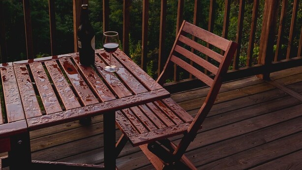 Terraza de madera con mesa y sillas, con vistas a un paisaje montañoso al atardecer.
