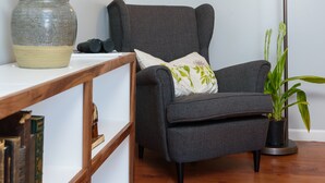 Una habitación con un sillón gris, una lámpara de pie, una estantería y una planta en maceta.