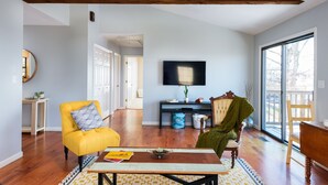 Un salón espacioso con pisos de madera, un sillón amarillo, una butaca verde, una mesa de centro de madera y un amplio ventanal con vistas al exterior.