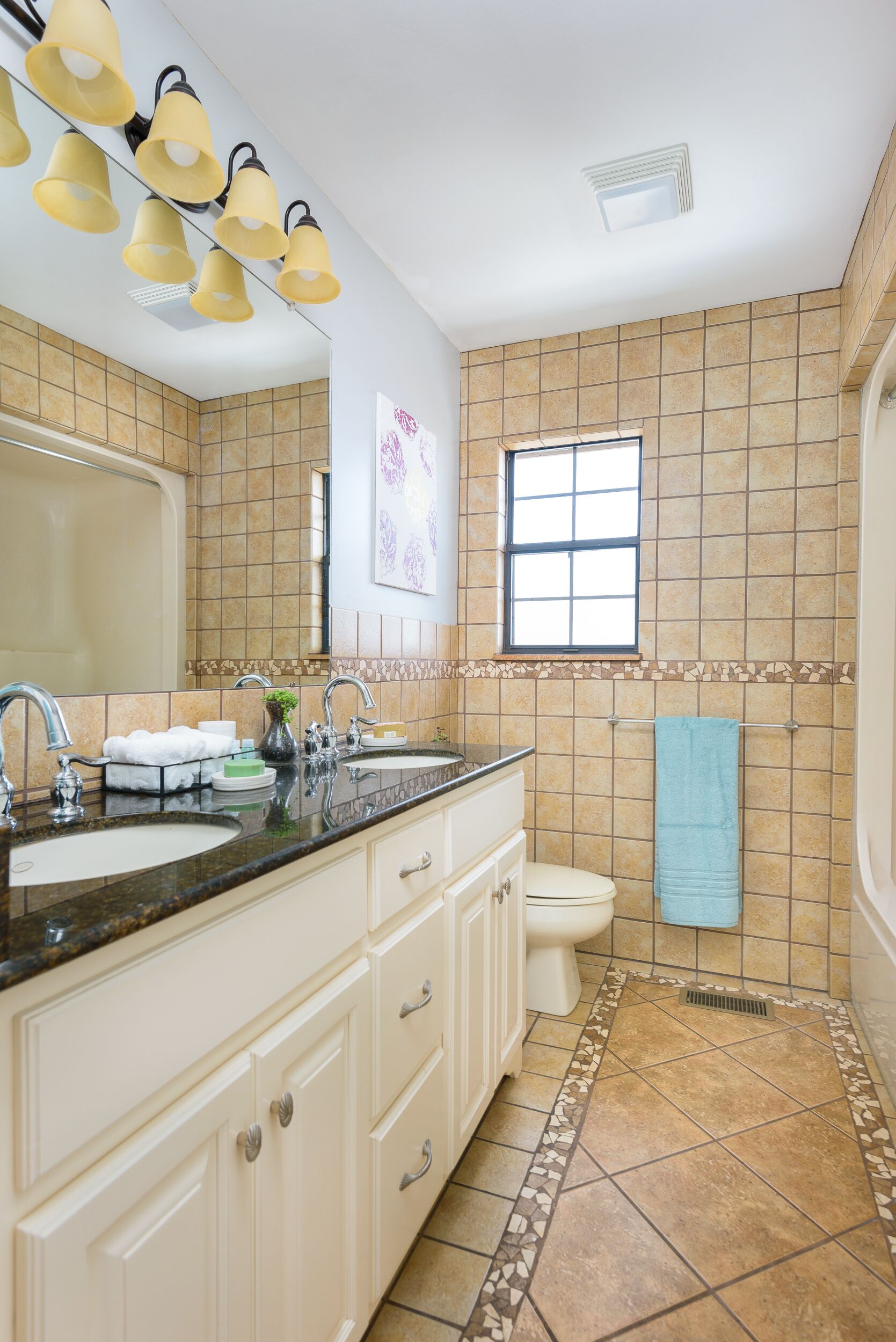 A bathroom with a large mirror, two sinks, a toilet, and a window.