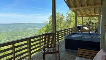 Une terrasse en bois avec un jacuzzi, une chaise et un canapé, le tout offrant une vue imprenable sur un paysage magnifique.