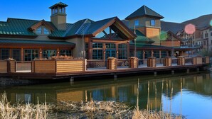 Un chalet au bord du lac, doté d’une terrasse en bois, de grandes fenêtres et d’un toit en métal.