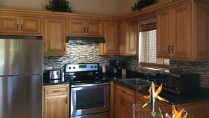 A kitchen with wooden cabinets, a stainless steel refrigerator, a black stove, and a window with blinds.