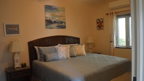 A bedroom with a large bed, two bedside tables, a ceiling fan, and a window with curtains.