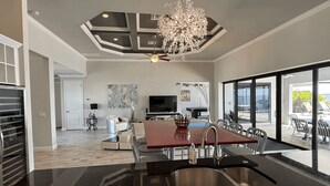 Een moderne keuken met een groot eiland, een eethoek met een rode tafel en uitzicht op een zwembad en terras.