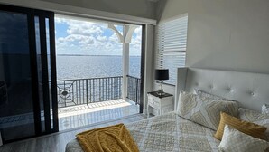 Een slaapkamer met een groot bed, uitzicht op zee en een balkon.