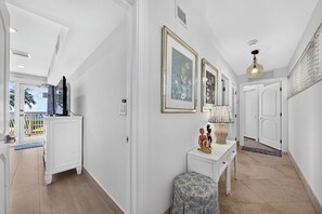 Un corridoio con pareti bianche, una porta bianca e un tavolino con oggetti decorativi.