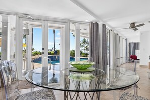 A modern dining area with a glass table and chairs, a view of a pool, and a ceiling fan.