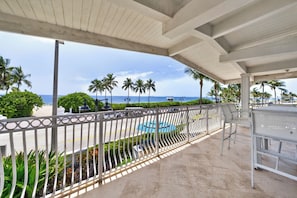 Área externa coberta com vista para a praia, palmeiras e piscina.