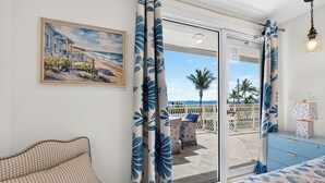 Una habitación con un sofá a cuadros, un cuadro con una playa y vista al mar a través de un ventanal.