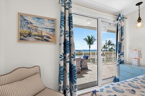 Una stanza con un divano a quadri, un quadro raffigurante una spiaggia e vista sul mare tramite una porta in vetro.