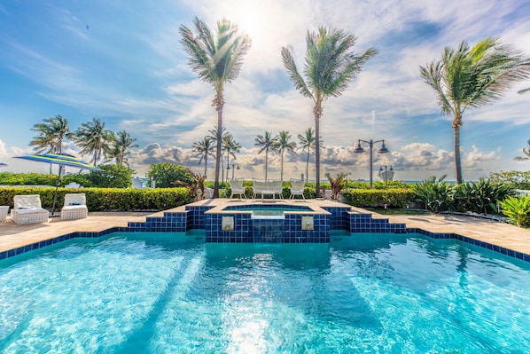 A swimming pool with blue tiles, surrounded by palm trees and lounge chairs.