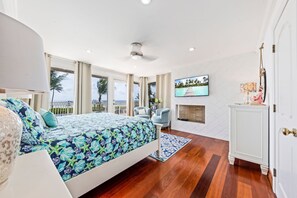 A bedroom with a bed, a TV, a fireplace, and a view of the ocean.