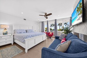 A bedroom with a bed, a sofa, a TV, and a ceiling fan.