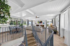 A spacious interior with a staircase leading to a balcony, large windows, and a fireplace.
