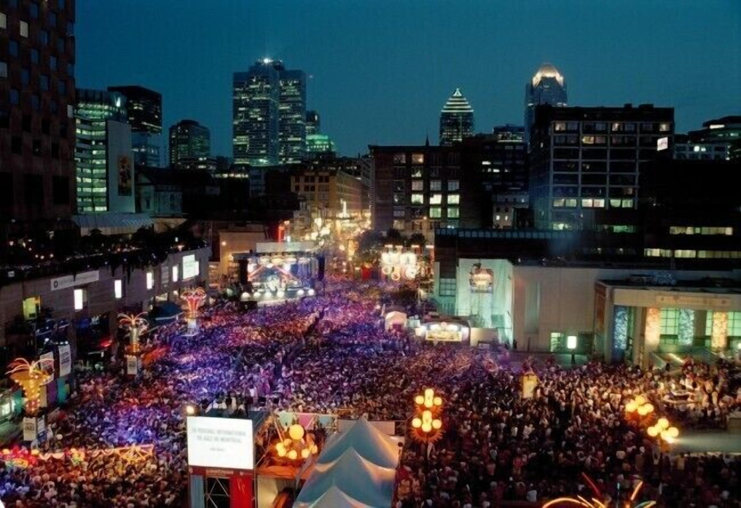 A crowded urban square at night with illuminated buildings in the background.