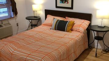 A neatly made bed with striped bedding, two bedside tables with lamps, a framed picture on the wall, and a window with blinds.