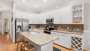 A modern kitchen with white cabinets, granite countertops, stainless steel appliances, and a wine rack. - 113 Waters Edge - Sunset Haven - Renovated Riverside Townhome - Pool & Fishing Pier (Folly Beach)