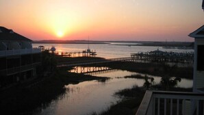 A waterfront property with a dock extending into the water, a pier, and a building with a balcony overlooking the scene. - 113 Waters Edge - Sunset Haven - Renovated Riverside Townhome - Pool & Fishing Pier (Folly Beach)