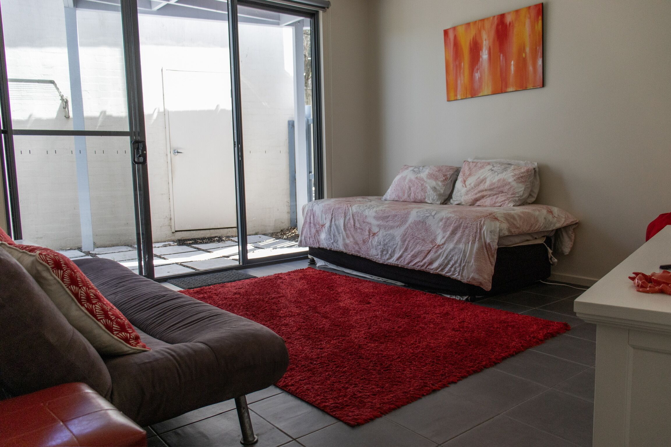 A bedroom with a bed, a red rug, and a sofa.