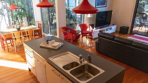 Uma cozinha moderna com uma ilha central, uma área de jantar com cadeiras vermelhas e uma sala de estar com sofá e televisão.
