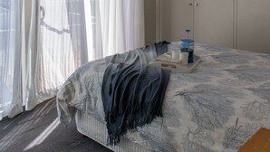 Quarto com cama, ventoinha no teto, janela com cortinas leves e guarda-roupa.