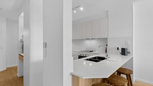 Una cocina moderna con armarios blancos, estufa negra, un fregadero y taburetes de madera.