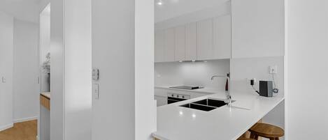 Una cocina moderna con armarios blancos, estufa negra, un fregadero y taburetes de madera.