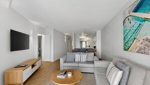 Una sala de estar moderna con un televisor de pantalla plana, una mesa de centro de madera y un sofá gris con cojines a rayas.