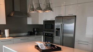 Une cuisine moderne avec des meubles blancs, des appareils en acier inoxydable et des luminaires suspendus.