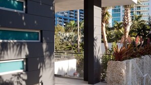 Un bâtiment moderne doté d’un balcon, de grandes fenêtres et offrant une vue sur des palmiers et une végétation luxuriante.
