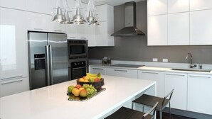 Une cuisine moderne avec des meubles blancs, des appareils en acier inoxydable et un îlot central agrémenté de fruits.
