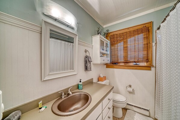 Baño con lavamanos, inodoro y ventana con persianas.