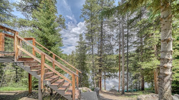 Una escalera de madera que sube a una plataforma en un área boscosa, con un lago al fondo.