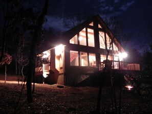 A house with a large glass window, a porch, and a fire pit in the yard.
