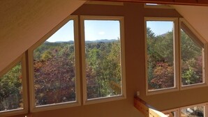 A room with a sloped ceiling and large windows offering a view of a forested landscape. - Unwind with Sautee Start Line, Hot tub, Firepit, Hammock, PS3 (Clarkesville)