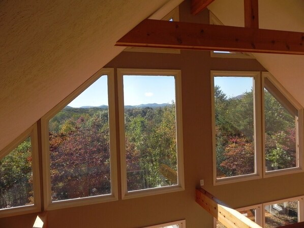 A room with a sloped ceiling and large windows offering a view of a forested landscape.