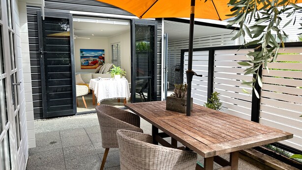 An open patio with a wooden table and wicker chairs, a potted plant, and an orange umbrella. - Black & White Retreat
 (Omaha Beach)