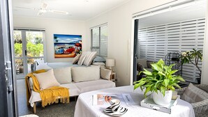 A modern bedroom with a bed, a bedside table with a cup and saucer, a potted plant, and a window with blinds. - Black & White Retreat
 (Omaha Beach)