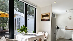 A modern kitchen with white cabinetry, a stainless steel refrigerator, and a dining area with wicker furniture and a white tablecloth. - Black & White Retreat
 (Omaha Beach)