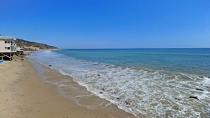 A beach with a clear blue sky, sandy shore, and a building with a lifeguard tower. - Exclusive Oceanfront Cottage on Dry Sandy Carbon Beach - Seal (Malibu)