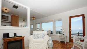 A spacious living room with a white sofa, a wooden entertainment unit, and a view of the ocean through large windows. - Exclusive Oceanfront Cottage on Dry Sandy Carbon Beach - Seal (Malibu)
