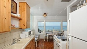A compact kitchen with wooden cabinets, a sink, a stove, and a dining table with chairs. - Exclusive Oceanfront Cottage on Dry Sandy Carbon Beach - Seal (Malibu)