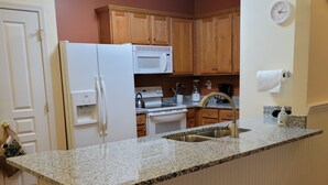 Una cocina con encimera de granito, armarios de madera, refrigerador, microondas y pileta.