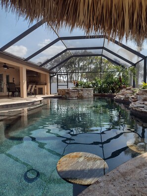 An indoor swimming pool with a glass ceiling, stone walls, and a seating area with chairs and a table.