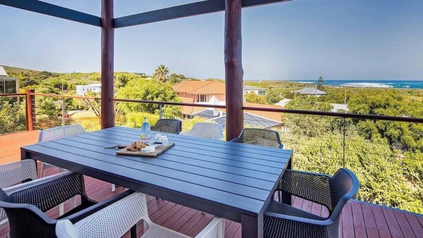 A covered outdoor seating area with a table and chairs, overlooking a coastal landscape.